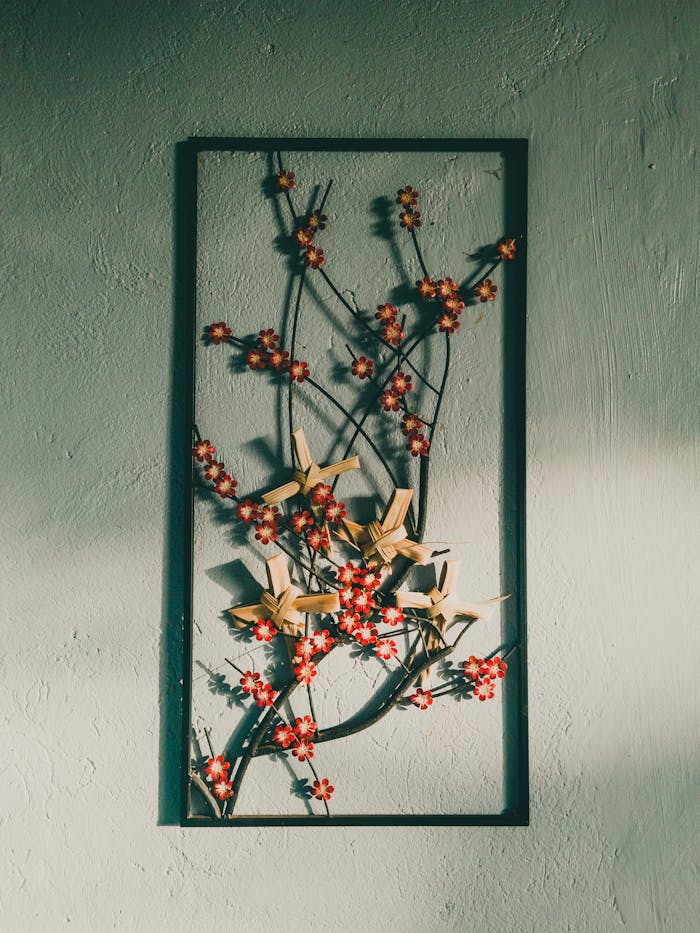 about-us Close-up of a decorative floral art piece with red blossoms in a frame against a textured wall.